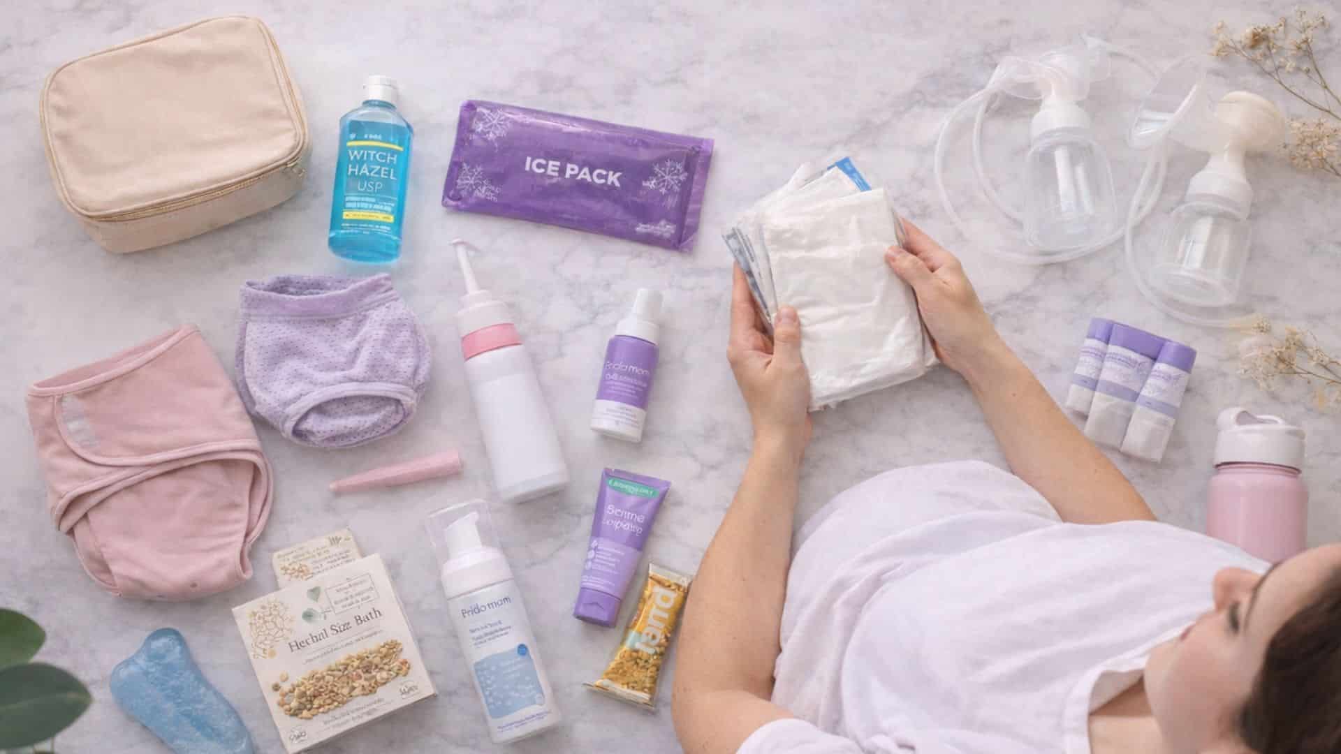 Produits essentiels de récupération post-partum disposés sur une surface claire, incluant culottes, soins apaisants, accessoires d’allaitement et indispensables du quotidien pour accompagner les premières semaines après l’accouchement.