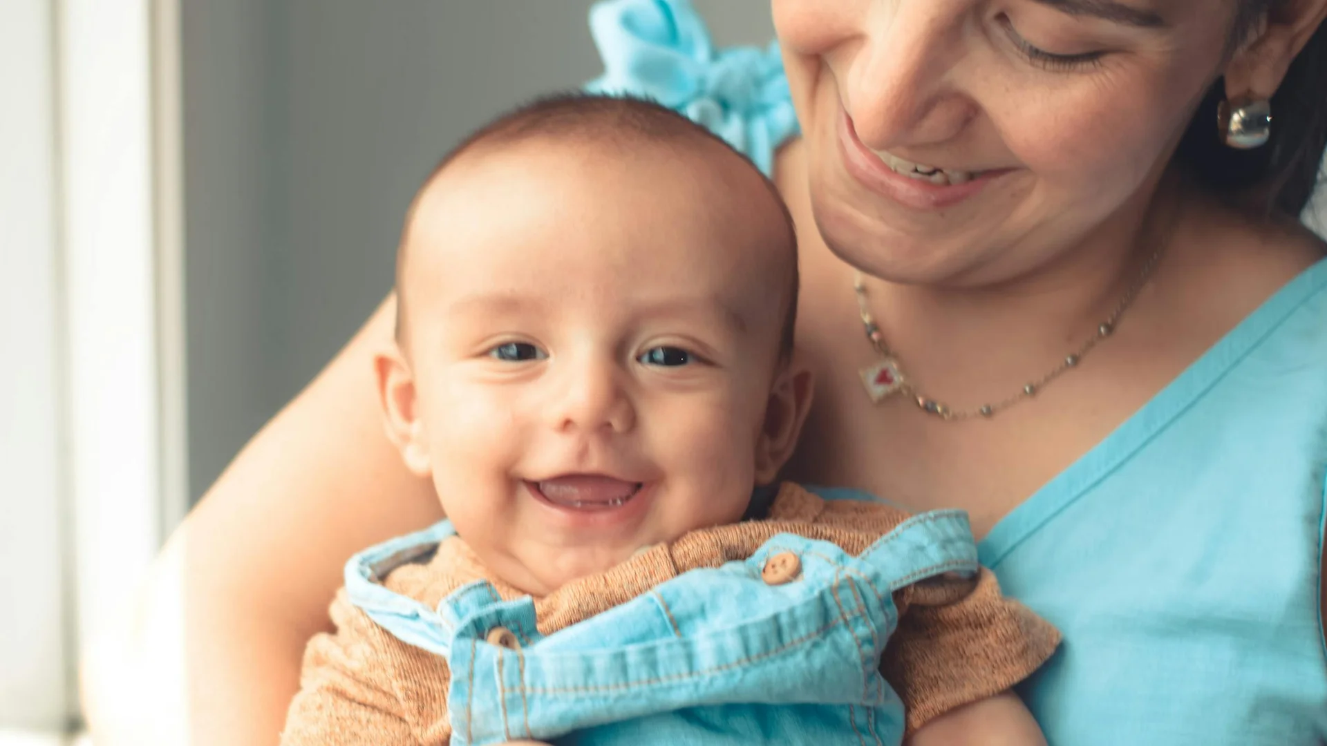 Jeune maman souriante tenant tendrement son bébé près d'une fenêtre lumineuse