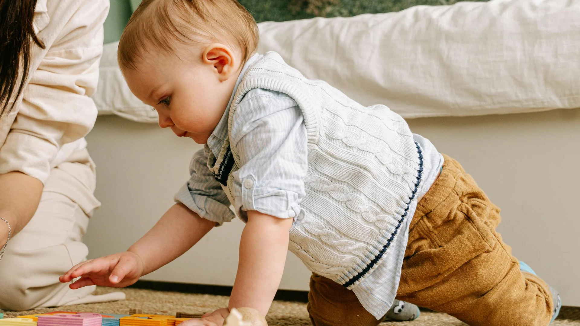 Bébé d'environ un an explorant des jouets éducatifs aux côtés d'une assistante maternelle attentionnée