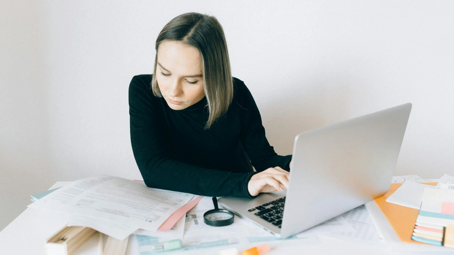 Jeune maman concentrée remplissant un formulaire administratif sur son ordinateur portable entourée de papiers