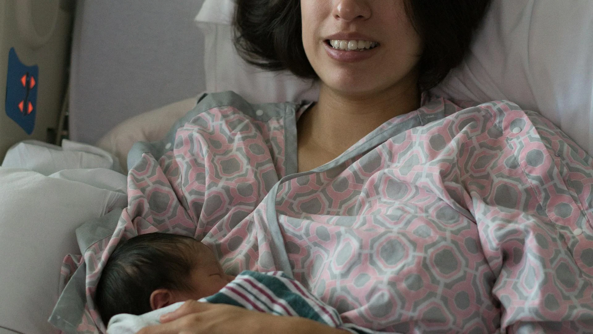 Femme en post-partum installée confortablement sur son lit avec des coussins, lumière douce d'une fenêtre