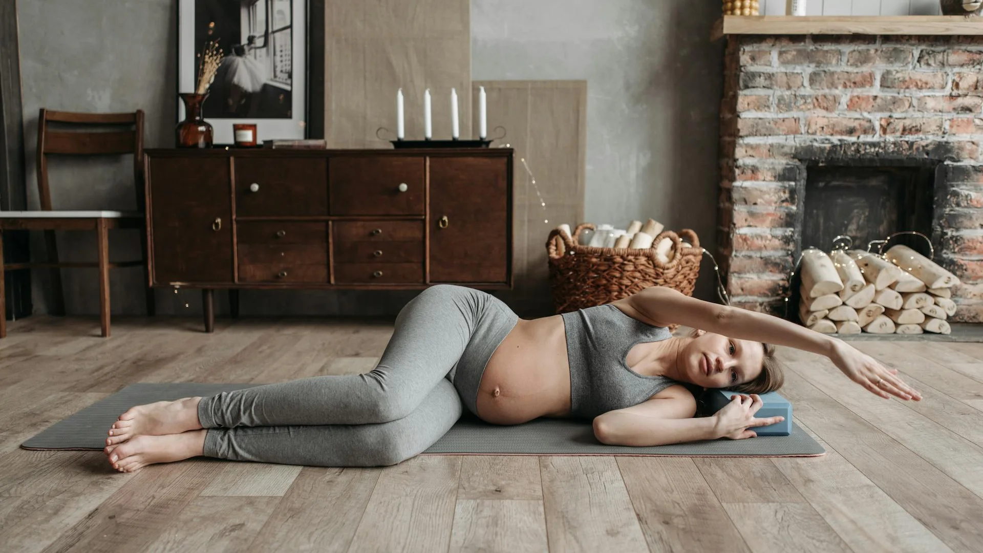 Femme enceinte allongée sur un tapis de yoga effectuant l'étirement du piriforme, cheville croisée sur le genou opposé