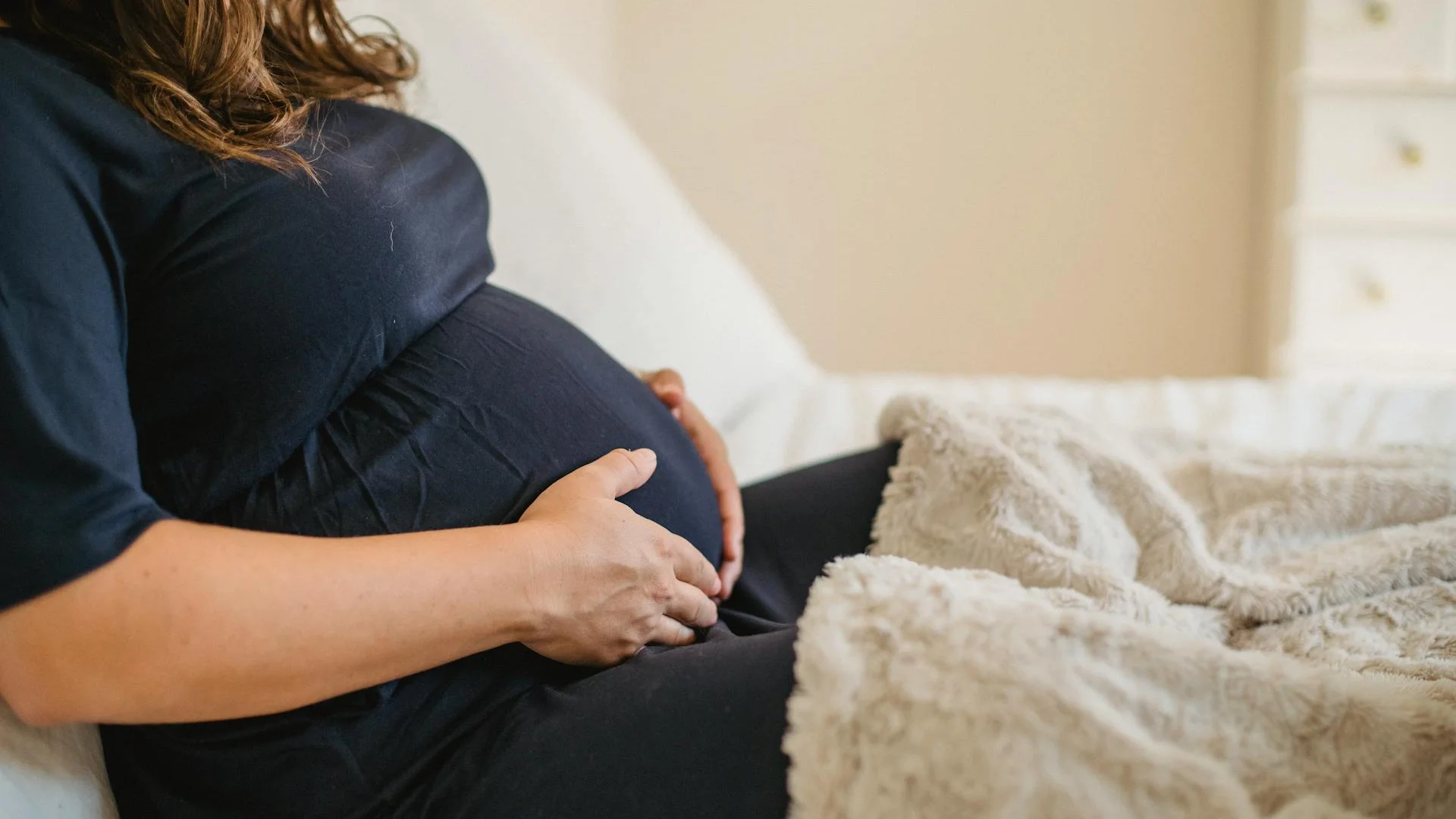 Femme enceinte dormant sur le côté gauche, un coussin de grossesse glissé entre les genoux et un petit coussin sous le ventre