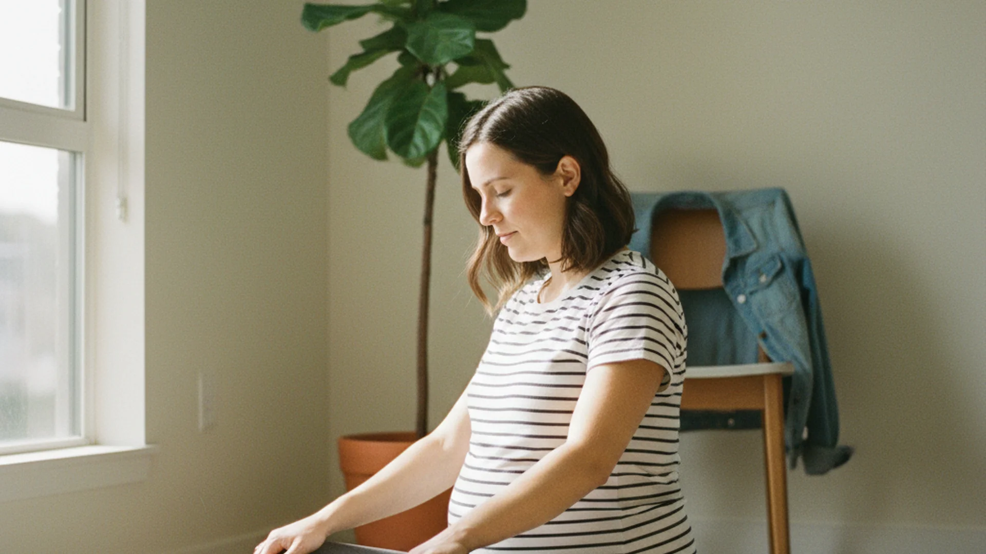 Femme enceinte au deuxième trimestre pratiquant la posture du papillon sur un tapis de yoga, assise près d'une fenêtre, lumière douce du matin, maison ordinaire en arrière-plan